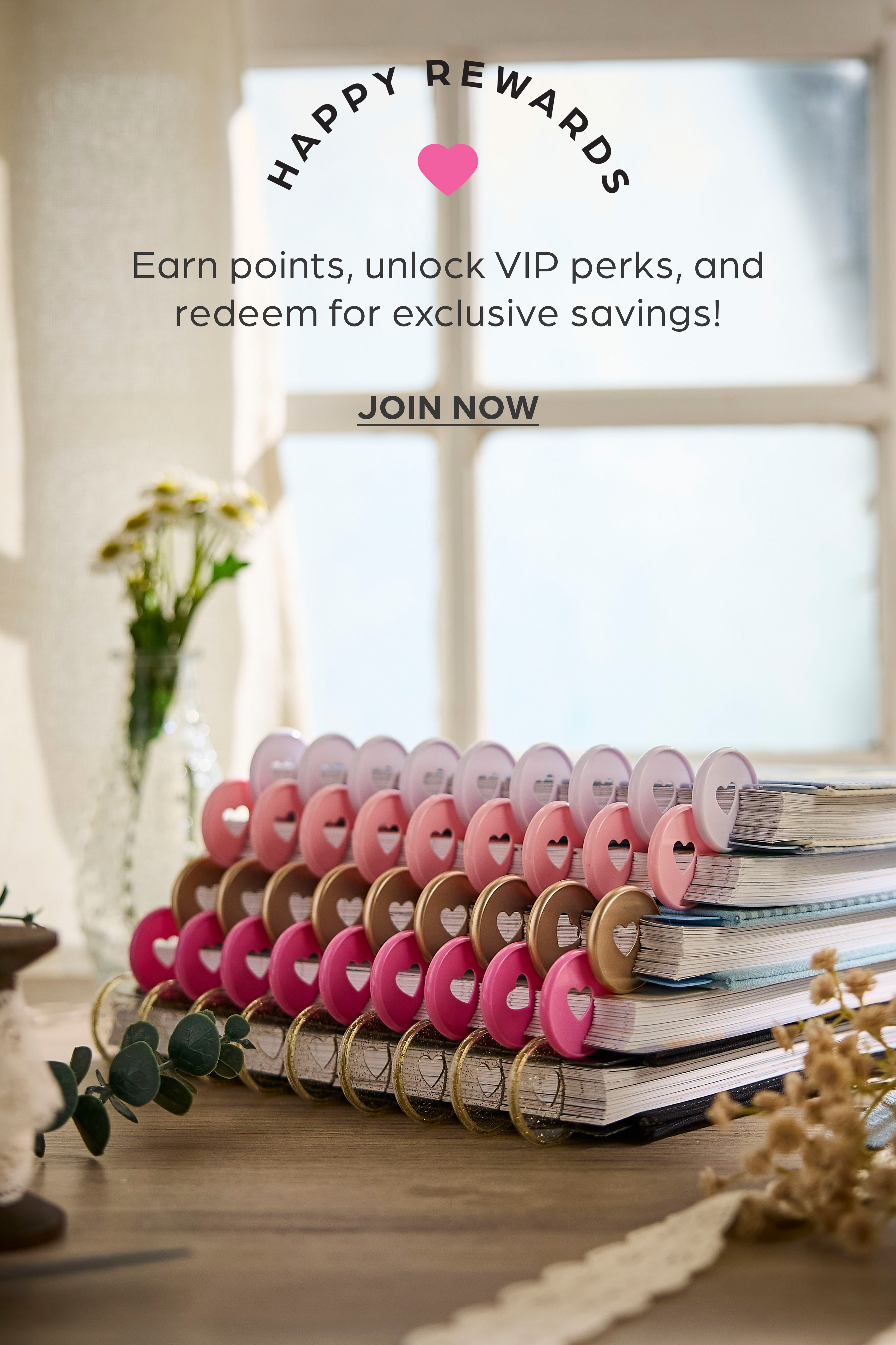 ```html
<img src=_image.html alt="Stack of notebooks with colorful covers and heart-shaped designs, promotional text for Happy Rewards program offering points, VIP perks, and savings. Decorative vase with flowers in the background." />
```
